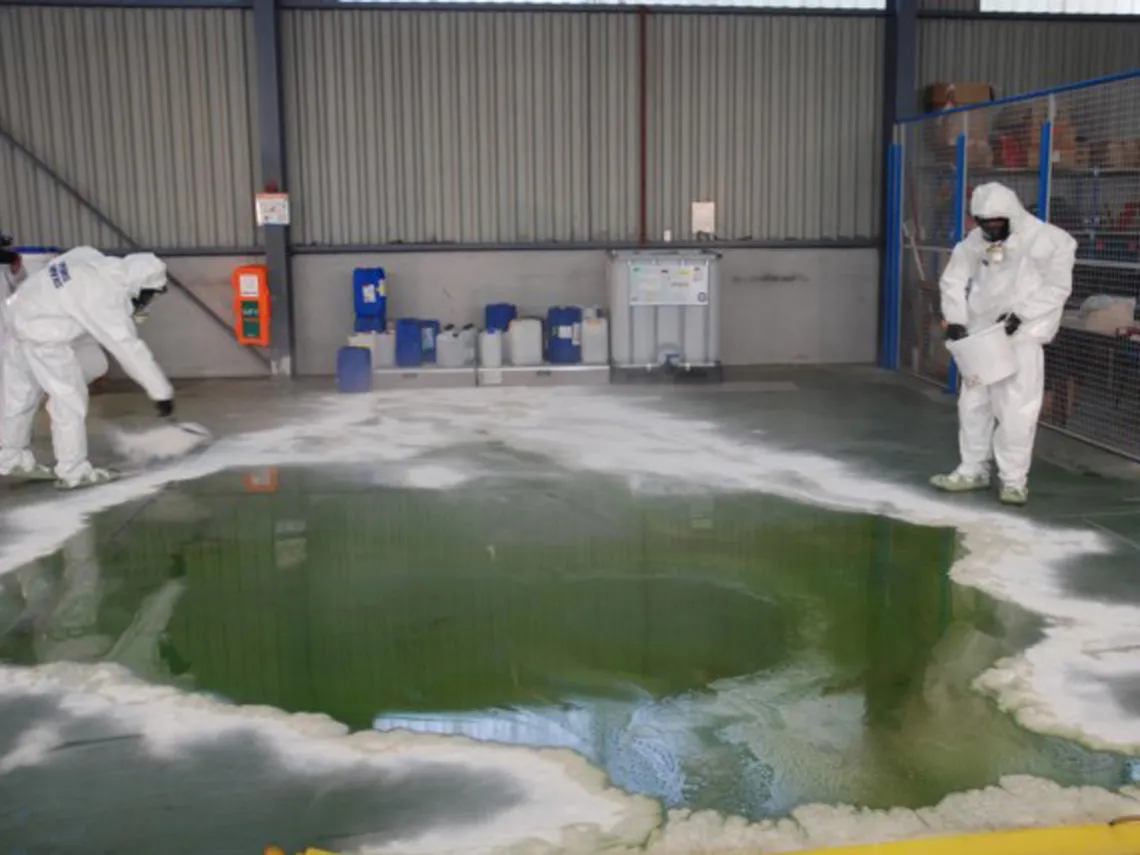 two employees in protective suits use a neutralizing absorbent during a major acid spill - chemical hazard